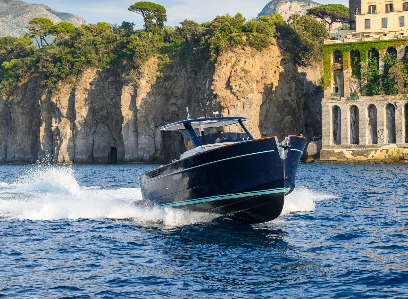 Un motoscafo scuro che sfreccia di fronte alla costa di Taormina