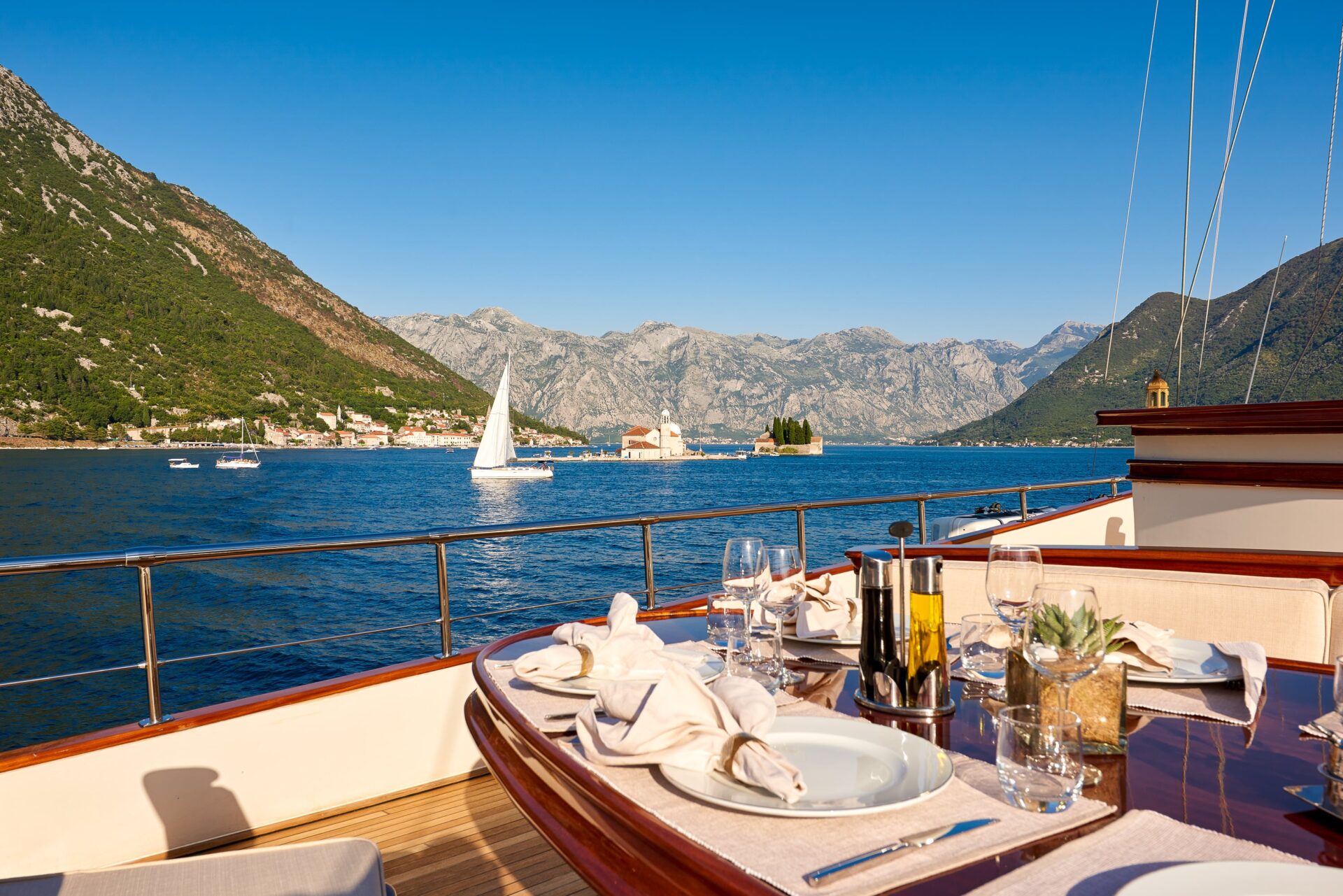 La foto di un tavolo elegantemente apparecchiato a bordo di una barca a vela di lusso con sfondo su panorama costiero italiano