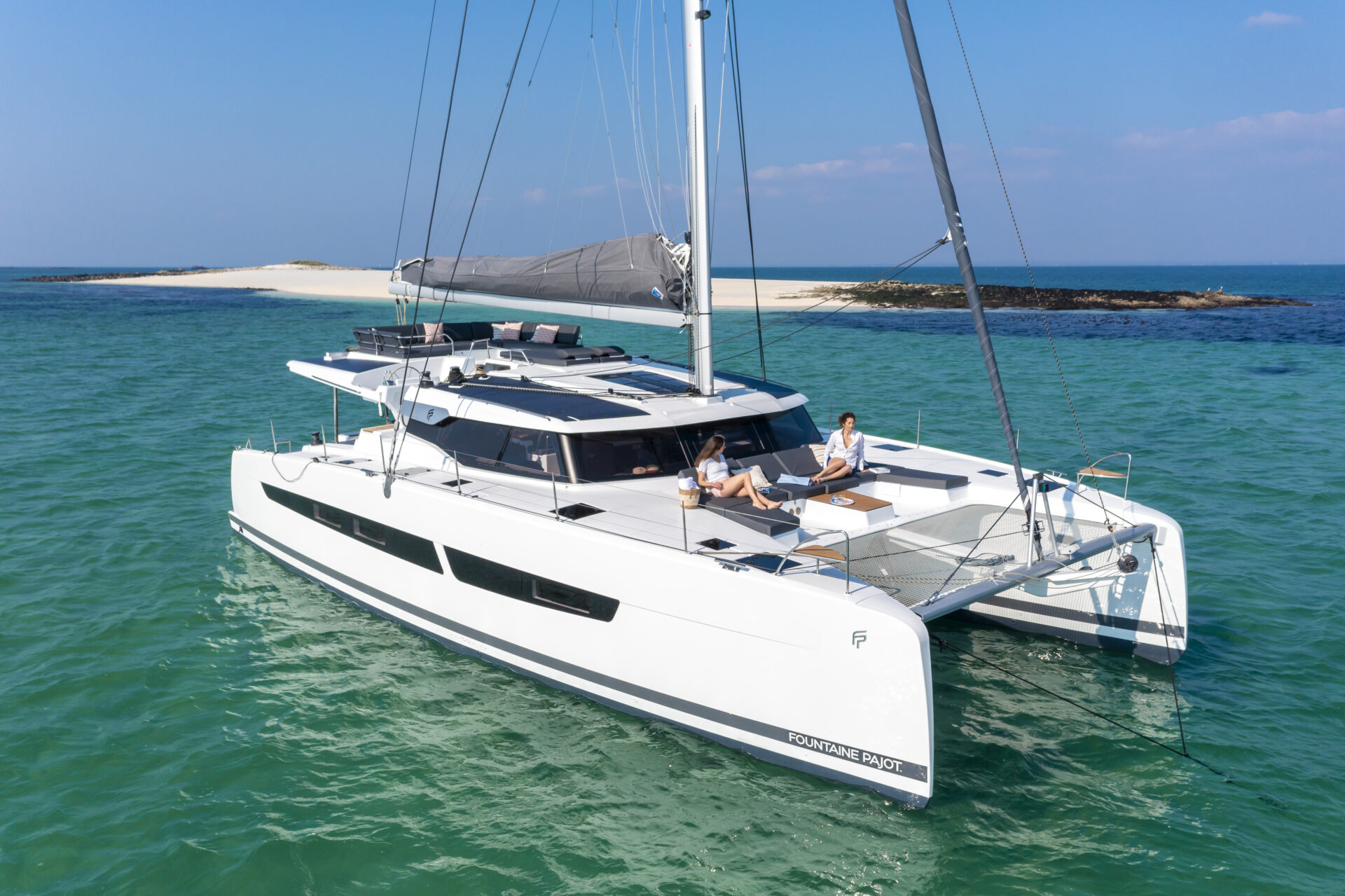 Due donne si rilassano su dei divanetti su un catamarano a vela di lusso in un mare verde acqua