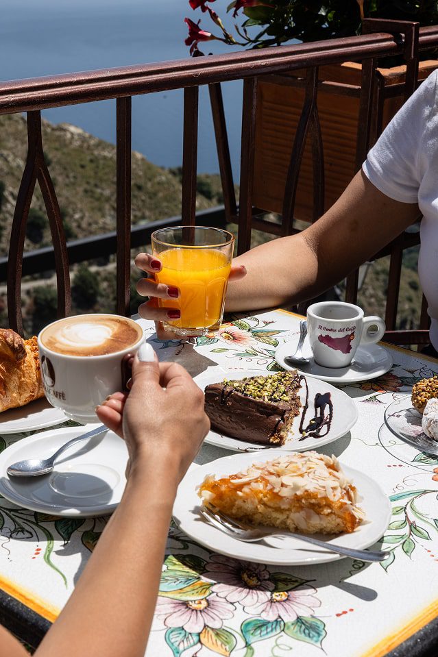 Tavolino imbandito con la tipica colazione all'Antico Bar Sangiorgio con cappuccino, succo d'arancia, cornetti e torte artigianali