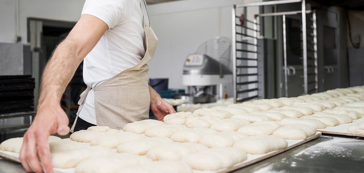Linea di produzione e lavorazione industriale di impasti per prodotti da forno con impastatrice professionale e carrelli porta teglie.