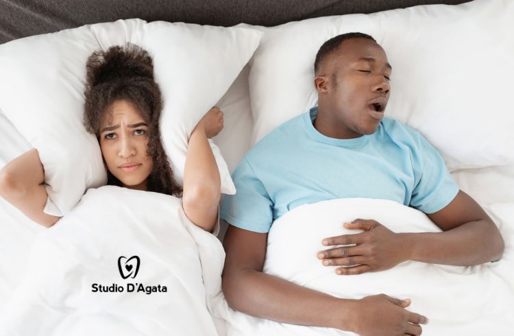 Un uomo è a letto e russa russa a causa delle apnee notturne. Accanto, la compagna si tappa le orecchie per il rumore