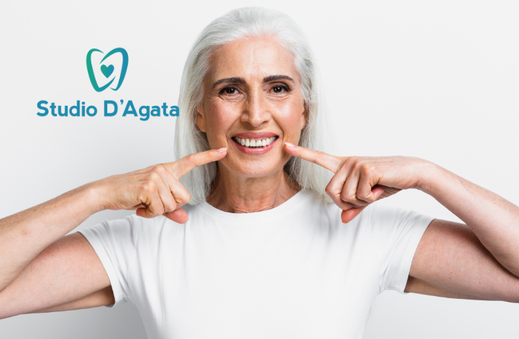 Una donna over 60 sorride indicando i suoi denti sani